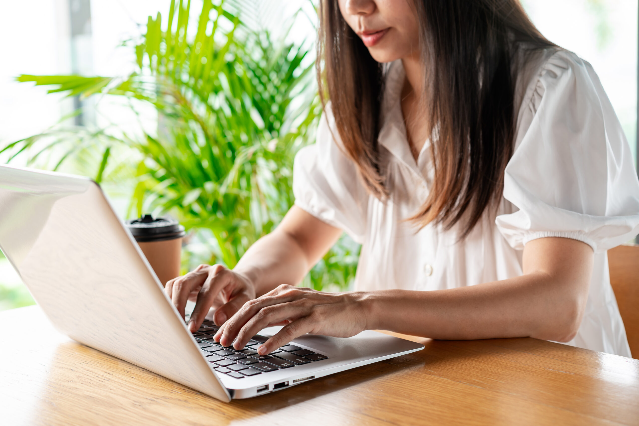 woman typing on her computer with a plant in the background