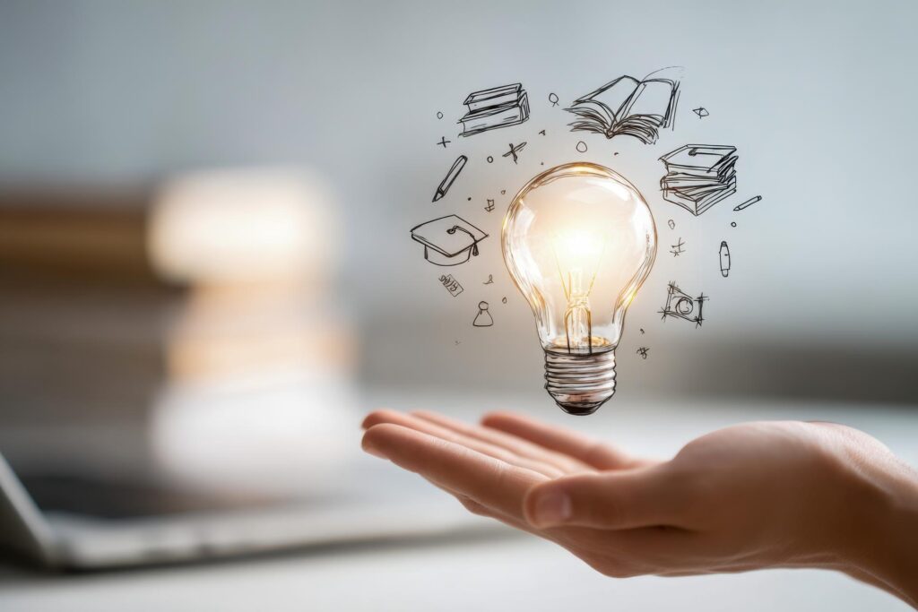 Hand holding glowing light bulb with education and knowledge icons floating around in a creative learning concept with blurred background